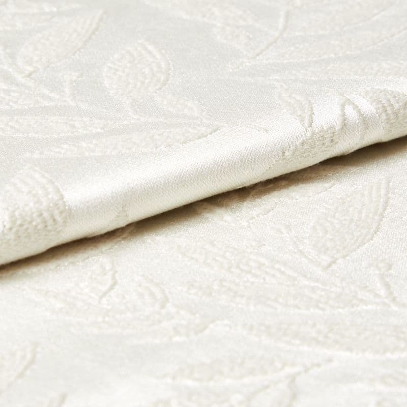 Cream damask fabric with raised floral pattern and satin sheen, shown folded and slightly overlapping; close-up view revealing textured embroidery and soft, diffuse lighting on a neutral surface.