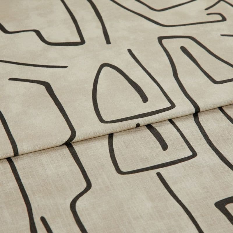 Beige linen-like curtain fabric with bold black abstract line pattern, hem visible; folded into a horizontal pleat; close-up in soft, neutral lighting showing fabric texture.