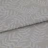 Beige-gray woven fabric with raised white botanical leaf pattern, folded once and layered, displaying texture and subtle sheen; close-up on textile surface under soft, neutral lighting.