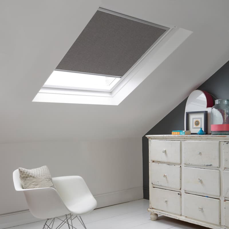 Room with white eaves wall, dark blue-grey wall to right with a shabby chic white drawer unit, a contemporary white chair, white painted floorboards and a skylight blind in mid slate grey.