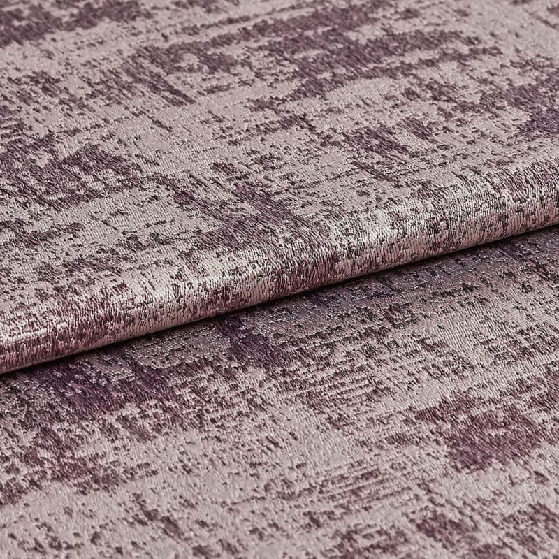 A folded roll of textured metallic mauve upholstery fabric with irregular crushed pattern — lying flat, photographed close-up under soft studio lighting to highlight its sheen.