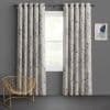 Grommet-top, leaf-patterned curtains hung on a metal rod, parted at the center and filtering soft daylight; framed by grey walls, a gold wire chair and abstract wall art.
