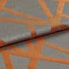 Woven gray-blue fabric with wide rust-orange geometric stripes, folded and overlapped; textured, slightly metallic sheen visible under soft studio lighting in a close-up view.
