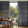 Dark textured pleated curtains, drawn aside centrally, framing an open glass door; daylight and a green garden visible beyond; foreground dining table set for breakfast beneath a pendant lamp.