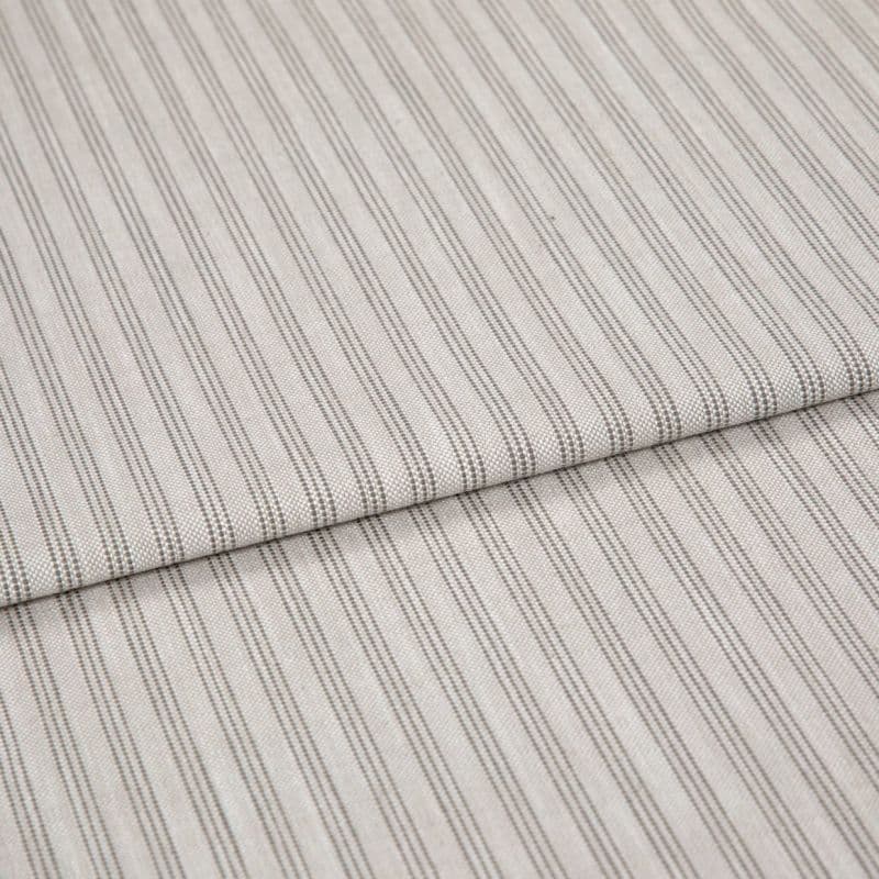 Beige woven fabric with thin vertical gray pinstripes, folded once and overlapping, lying flat as a sample in soft, diffuse lighting—close-up view emphasizing texture and pattern.