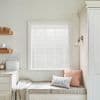 White horizontal venetian blinds (slatted, closed) covering the window, filtering soft daylight; bright neutral kitchen nook with cushioned bench, throw, wall sconce, countertop and bread box.
BREAD
THE PIG
