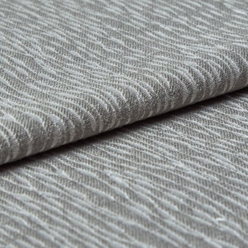 Folded grey woven fabric with raised, wavy ribbed texture (object) layered across itself (action) in a close-up, neutral-lit studio view emphasizing tactile detail (context).