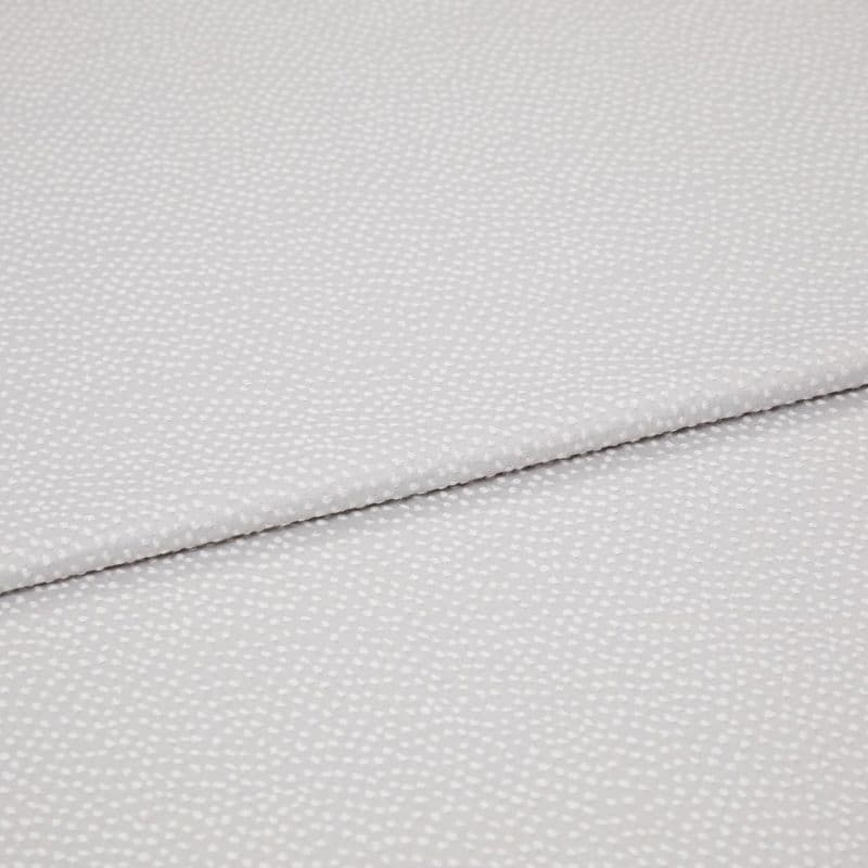 Light-gray fabric with small white dotted texture, folded diagonally with an overlapping edge; close-up view on a plain surface under soft, even lighting.