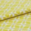 Folded yellow-green jacquard fabric with cream embroidered interlocking petal motif, close-up on a flat surface with bright even lighting, presented as a textile sample for upholstery or curtains.