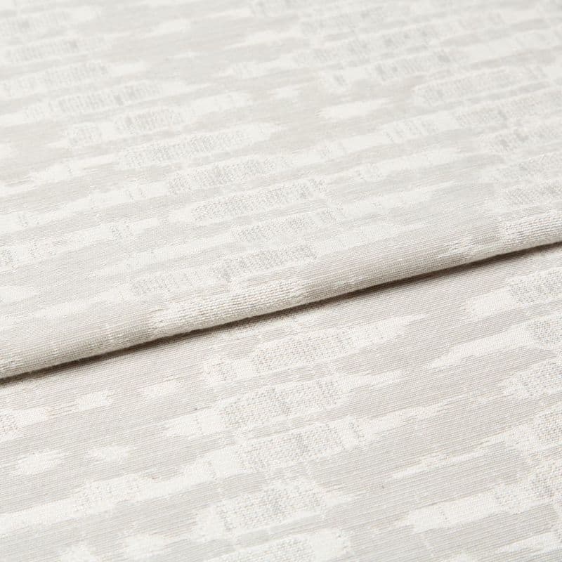 Off-white woven curtain fabric folded horizontally, showing a subtle geometric jacquard pattern; soft, diffused light highlights the texture in a neutral, close-up interior view.