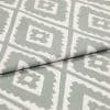 Folded woven fabric featuring repeating jagged-diamond, Aztec-like motif in sage green and off-white — layered across itself, lying flat in a soft, evenly lit close-up highlighting weave texture.