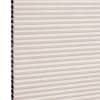 Beige pleated honeycomb cellular blind, fully lowered with visible black cells along the left edge; filtering light in a close-up studio view of the shade surface.
