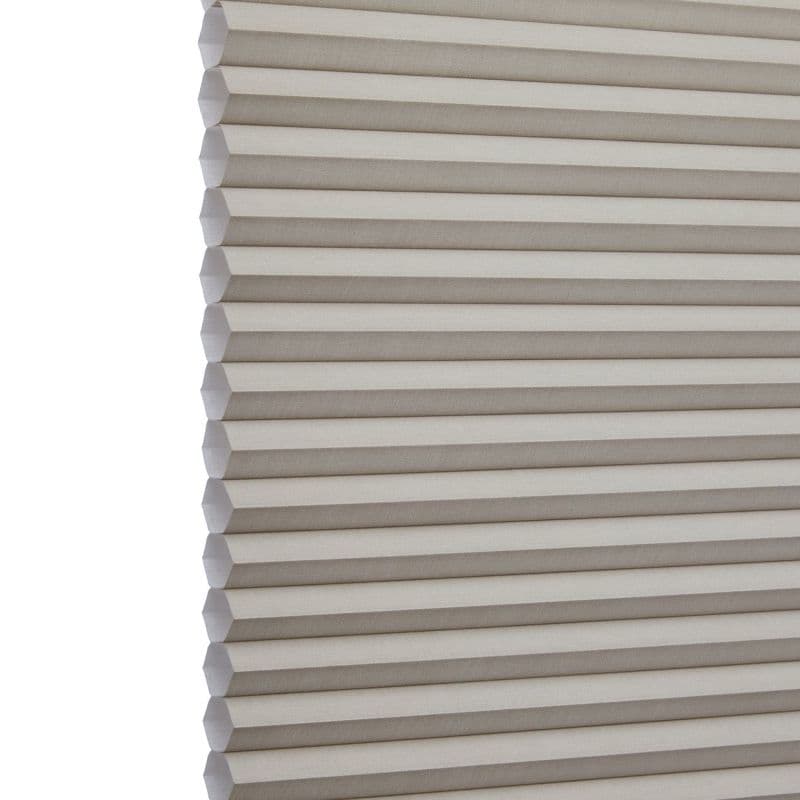 Cellular (honeycomb) window shade, beige pleated fabric hanging fully lowered with hexagonal cells, closed and gently filtering light; close-up interior view focusing on repeating horizontal folds.