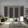 Dark roller blinds on four French door panes and sidelights, partially lowered blocking light with a gap revealing lawn, in a living room with sofas, glass table, chevron rug.