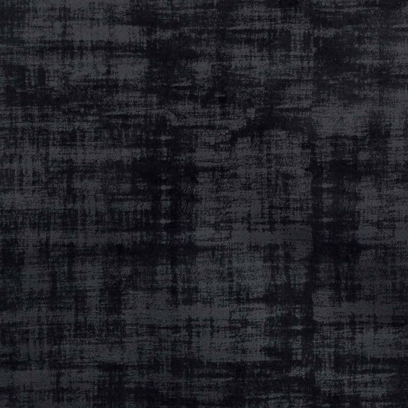 Dark charcoal fabric with a distressed, crosshatched texture (velvet-like), lying flat; displaying uneven shading and a worn appearance in diffuse, low-contrast lighting, like an upholstery or rug sample.