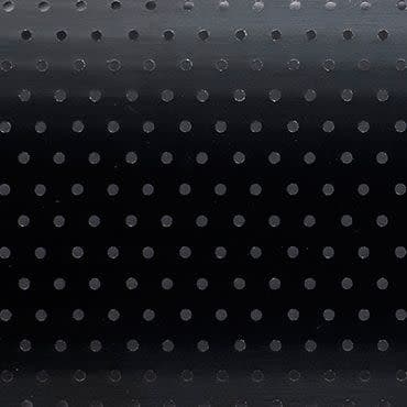 Black roller blind with regular small circular perforations — lowered and closed, the holes subtly admit faint light — set in a dim interior against a smooth background with a gentle top gradient.