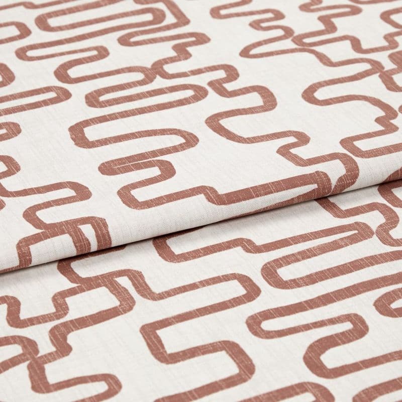 Folded off-white linen fabric printed with rust-colored, continuous squiggle pattern; fabric is layered and slightly creased, shown in close-up under soft studio lighting.