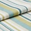 Woven striped fabric (teal, light blue, lime, white) folded in overlapping layers, displaying textured knit and rounded edges, close-up studio shot with soft, even lighting on a neutral surface.