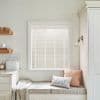 White horizontal venetian blinds covering the window, fully lowered with narrow slats filtering soft daylight; kitchen nook with built-in bench, patterned cushions, throw, wooden shelves, bread box, sconce.
BREAD