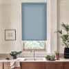 Blue roller blind covers most of a window, blocking light; kitchen sink with chrome faucet on marble countertop, wooden cabinets below, nearby potted plants, bowl of greens and framed sketch.