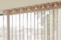 Sheer beige wave-headed curtains (ripple-fold) — hanging full-length, forming soft vertical pleats — filtering bright daylight into an interior living space, partially revealing blurred houses and trees outside.