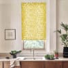 Yellow floral roller blind covers window, filtering light; above kitchen sink with stainless faucet, countertop, bowls of leafy greens, potted plants and framed sketch on the wall.
