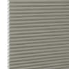 Gray-beige cellular honeycomb blind, pleated with visible hexagonal cell edges at left, closed and filtering light; close-up view with neutral, evenly diffused lighting and no visible room.
