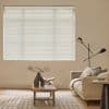 White horizontal blinds fully lowered and closed, softly filtering daylight through slats; beige living room with a neutral sofa, wooden coffee table, patterned rug and black floor lamp.