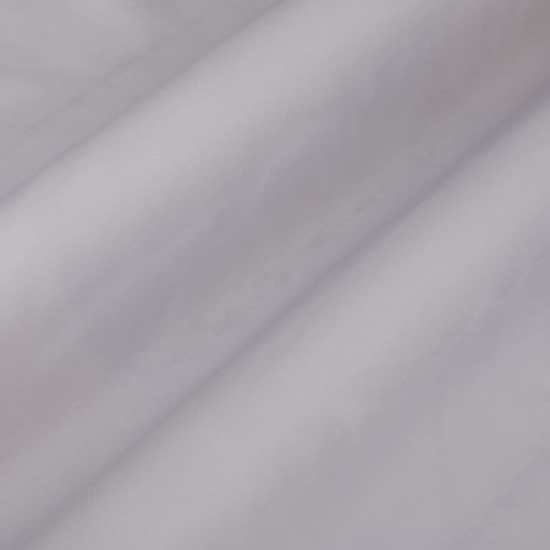 Pale lavender curtain fabric, hanging in soft diagonal folds, gently diffusing light in a neutral, dim interior close-up.
