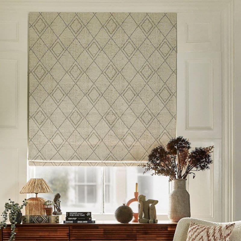 Beige fabric Roman blind with stitched diamond pattern, lowered to cover the window and softly filtering daylight. Beside a wooden console with lamp, books and a vase of dried flowers.
HOMES FOR OUR TIME
EVERYTHING ABIGAIL AHERN