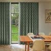 Panel curtains (green-and-cream checkerboard), floor-to-ceiling, mostly closed with a narrow central gap revealing a tall window and grassy yard; dining table with beige chairs and a teapot on a runner.