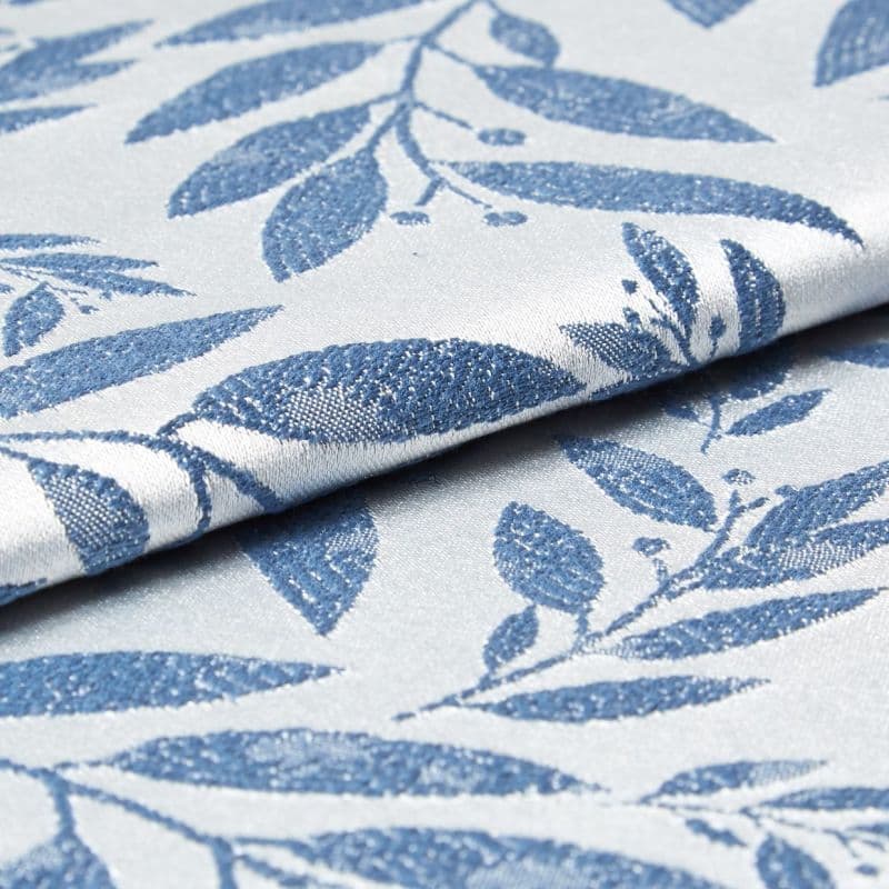 Folded woven fabric with raised blue leaf jacquard pattern; folded and overlapping, revealing textured weave and subtle sheen; close-up product-style shot with soft, neutral lighting suggesting upholstery or curtain material.