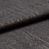 Dark gray woven fabric with slubs and subtle metallic threads; folded into a layered edge; tight macro close-up on a softly lit surface, neutral background suggesting an upholstery sample.