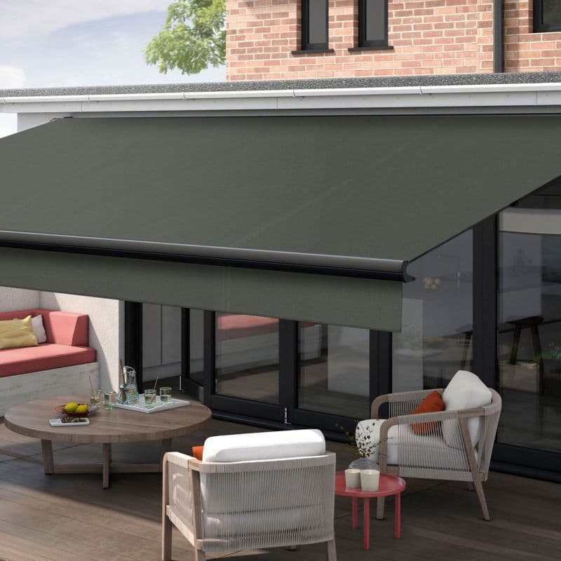 Dark green retractable awning with metal front bar and straight valance, fully extended over glass patio doors, shading a modern outdoor seating area with sofa, chairs, and coffee table, daytime.