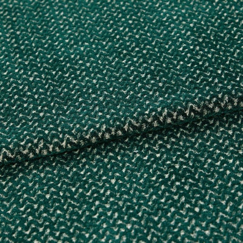 Green boucle-like fabric with dense cream zigzag pattern, folded into overlapping layers; close-up macro view on a neutral surface with soft, even lighting emphasizing the texture.