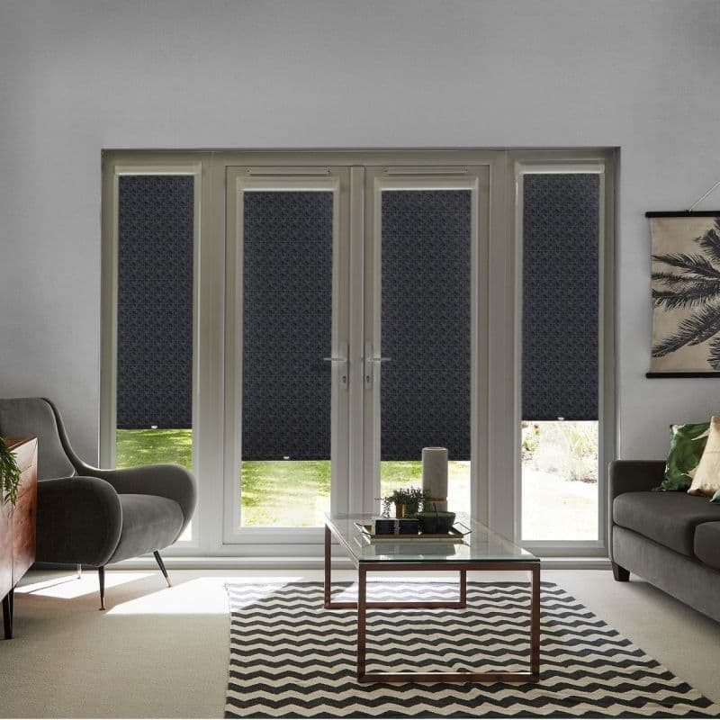 Dark patterned roller blinds on four-panel French doors and narrow sidelights, lowered to mid-height, filtering light; living room with gray seating, glass coffee table, chevron rug and a garden view.