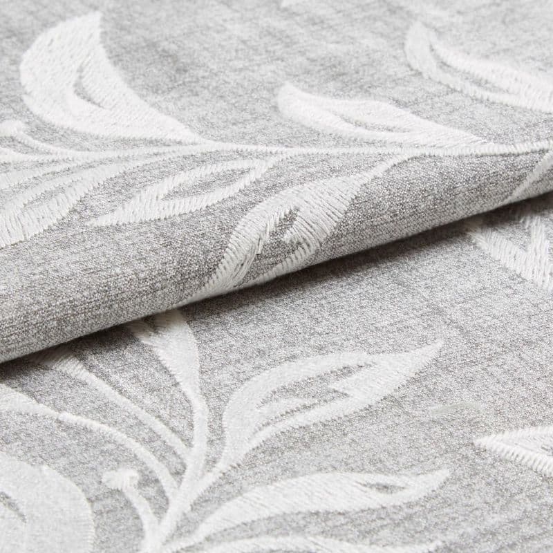 Textured gray fabric with raised white leaf embroidery folded and partially rolled, overlapping; close-up studio-lit view highlighting the weave and embossed botanical pattern.