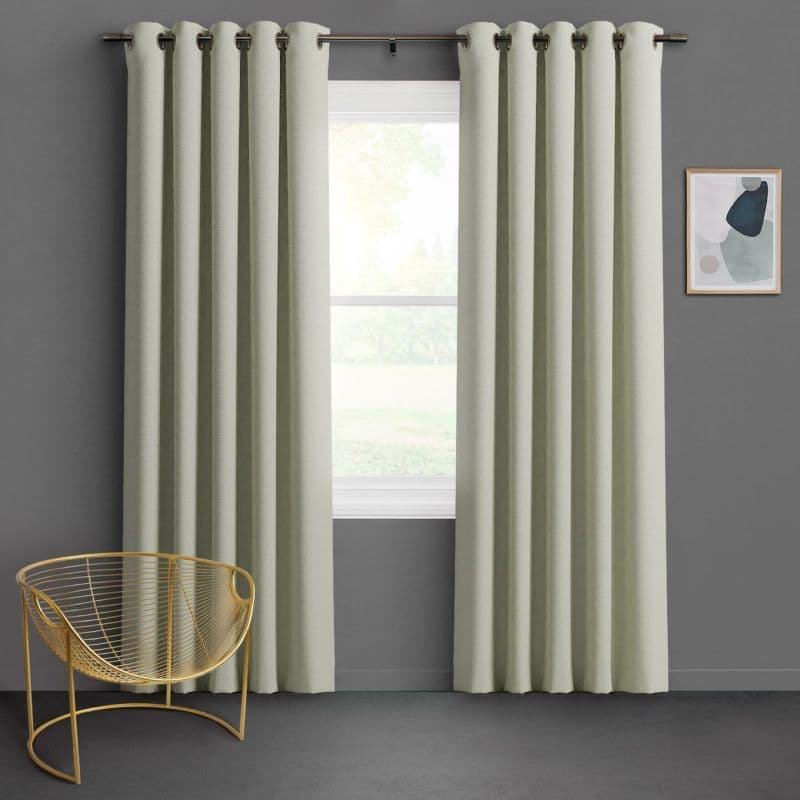 Grommet-top pale sage curtains, floor-length with deep pleats, hung on a metal rod and parted slightly, filtering soft daylight over a gray-walled room with gold wire chair and abstract art.
