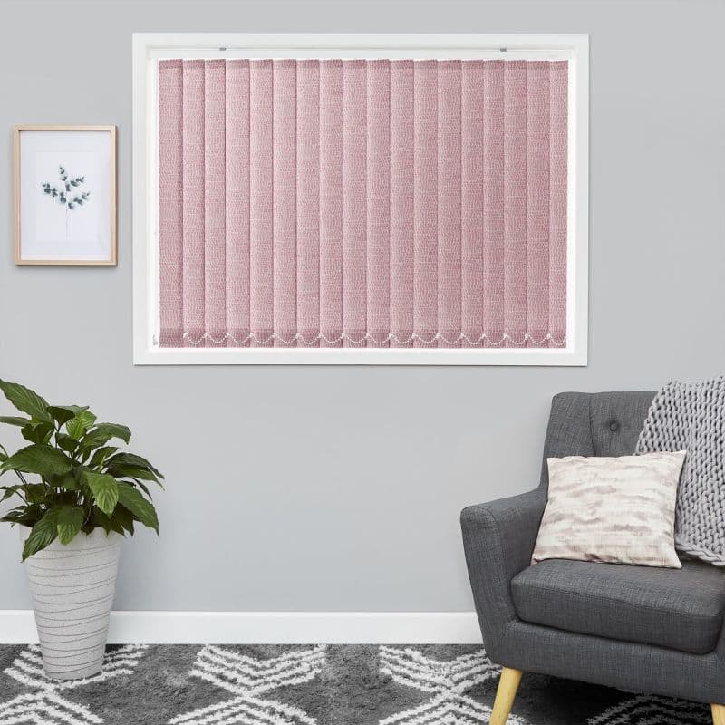 Pink textured vertical blinds cover the window fully, closed and softly diffusing daylight. In a gray living room with framed botanical art, potted plant, patterned rug and armchair with cushion.