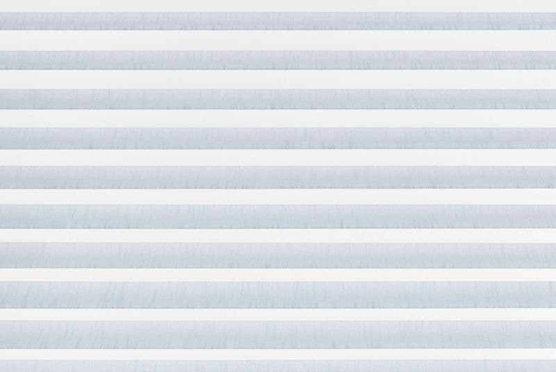 Horizontal zebra blinds with alternating white opaque and pale blue translucent fabric filling the frame, closed and filtering soft daylight, in a minimal interior with no visible view.