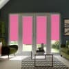 French doors and side windows with bright pink roller blinds lowered, facing a living room with green velvet armchairs, glass coffee table on a chevron rug and several houseplants.