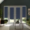 French doors with dark blue roller blinds, partially lowered over glass, in a cozy living room with green armchairs, glass coffee table on black-and-white chevron rug, garden beyond.