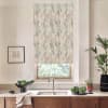 Patterned roller blind hangs down, partially covering a window above a kitchen sink; stainless faucet, wooden cabinets, potted plants and a framed sketch sit on the light countertop.
