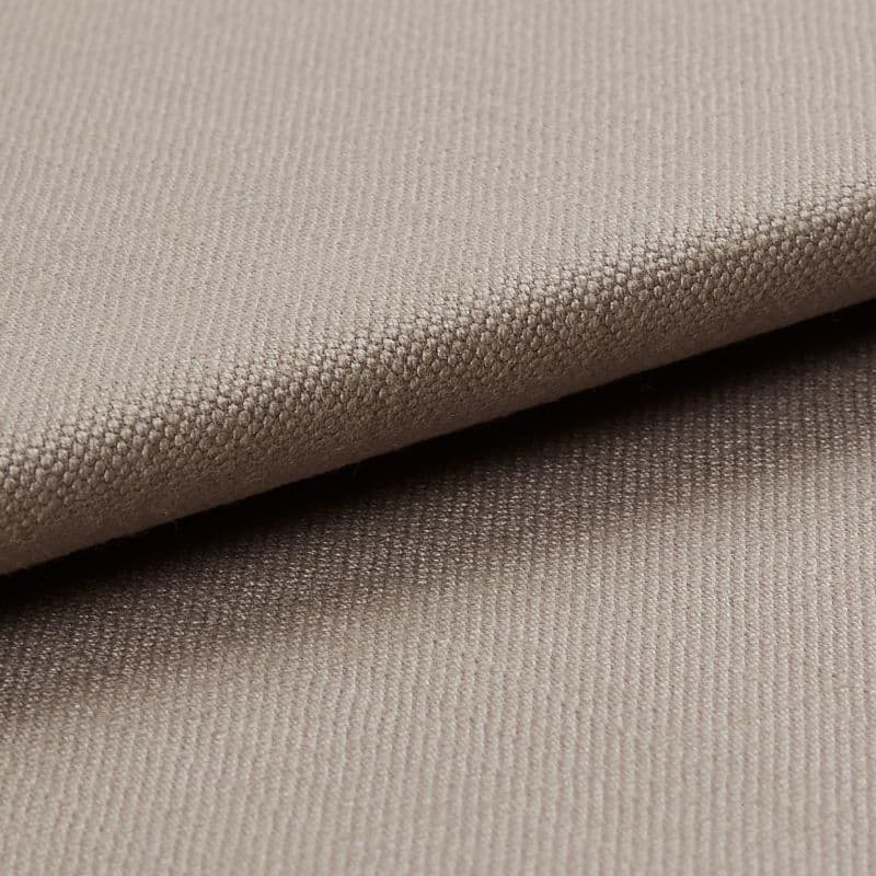 Beige tightly woven upholstery fabric, folded with an overlapping edge across the frame, revealing a pebble-like weave; close-up macro view with soft neutral lighting and plain background.