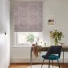 Roman blind with mauve circular-dot pattern, lowered over the window and filtering daylight; a desk and teal chair face the window in a home office with a vase of flowers.