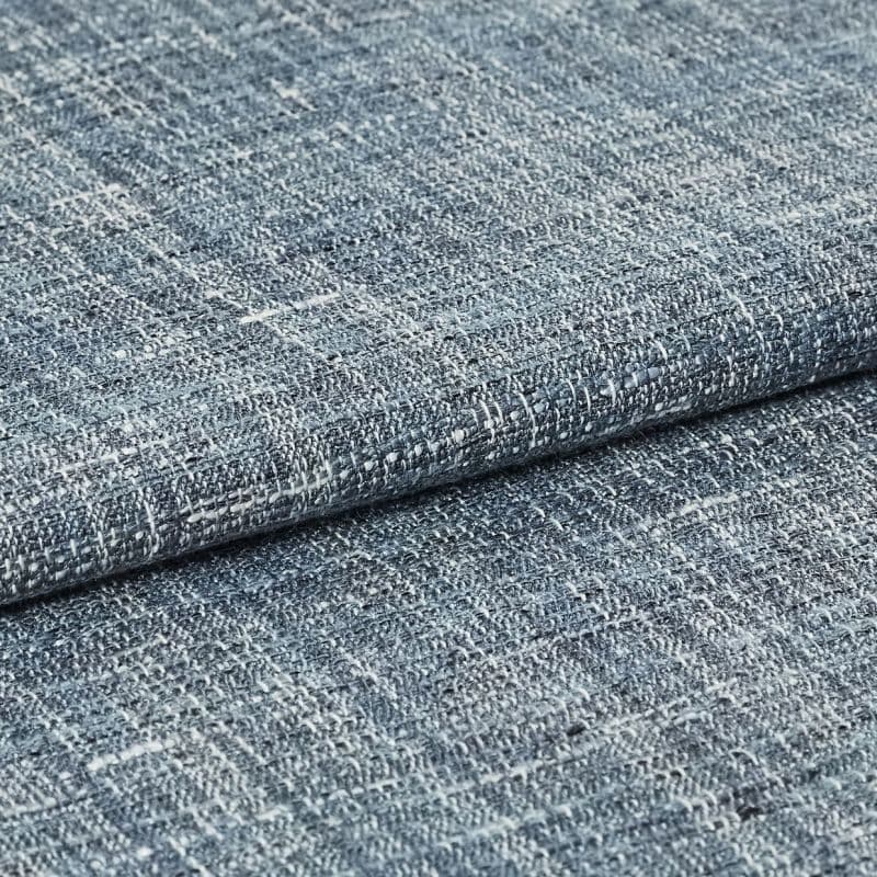 Blue-gray woven fabric swatch with irregular white flecks — folded and overlapped — close-up studio view with even lighting, emphasizing coarse looped weave and subtle color variation.