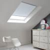Room with white eaves wall, dark blue-grey wall to right with a shabby chic white drawer unit, a contemporary white chair, white painted floorboards and a skylight blind in pale blue.