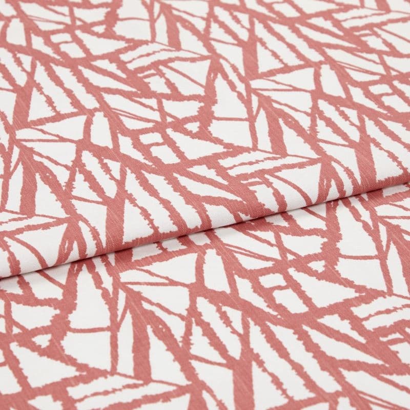 White fabric with coral-pink angular, brushlike linear pattern, folded over itself; fabric lies flat, close-up studio view showing texture and repeating print.