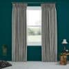 Grey pleated floor-length curtains on a metal rod, flanking and drawn aside to reveal a bright double-hung window, filtering soft daylight in a teal-walled room with carpet, lamp, and plants.