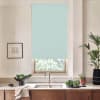 A pale blue roller blind covers most of a kitchen window, hanging above a stainless sink on a light countertop, flanked by potted plants, wooden cabinets, and a framed wall sketch.